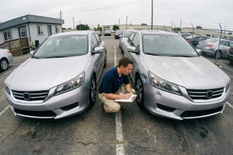 Deux voitures identiques côte à côte dans un parking de concessionnaire, examinées par un expert automobile tenant un clipboard pour comparer leur cote