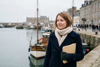 Femme regardant la mer à Cherbourg avec un manteau bleu