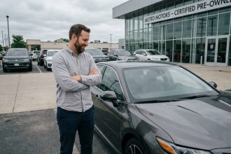Homme examinant une voiture d'occasion récente dans un parking de concession automobile