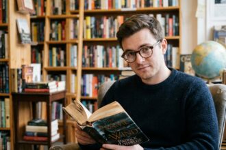Jeune homme portant des lunettes rondes en écaille de tortue lisant un roman fantasy dans une librairie indépendante vintage